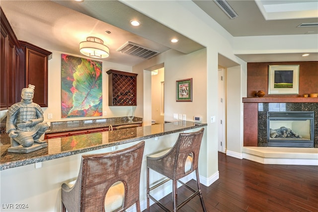 kitchen with kitchen peninsula, a breakfast bar area, dark stone counters, dark wood-type flooring, and a fireplace