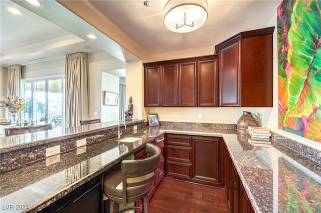 kitchen featuring sink, kitchen peninsula, dark hardwood / wood-style floors, and dark stone countertops