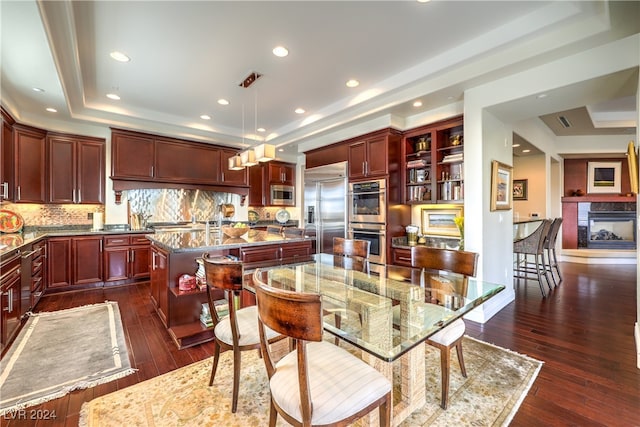 kitchen featuring a kitchen island, a premium fireplace, dark hardwood / wood-style floors, built in appliances, and decorative light fixtures