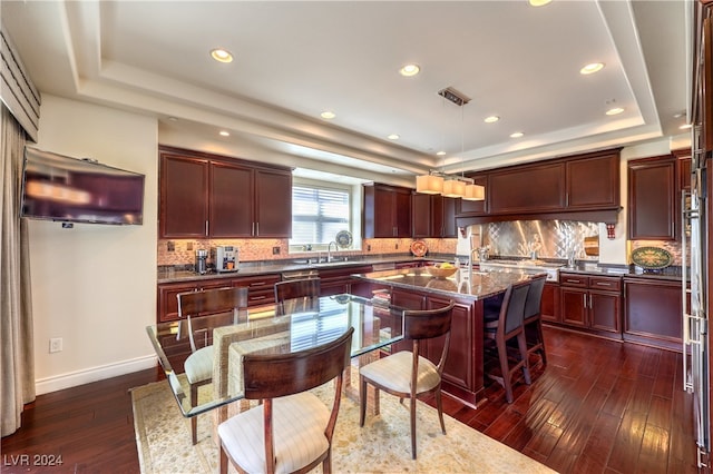 kitchen with decorative backsplash, a kitchen island, a tray ceiling, dark stone countertops, and dark hardwood / wood-style floors