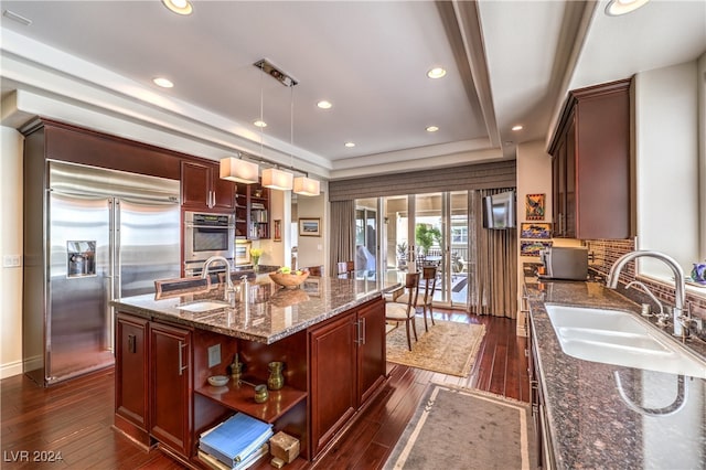 kitchen with built in refrigerator, sink, a kitchen island with sink, and decorative light fixtures