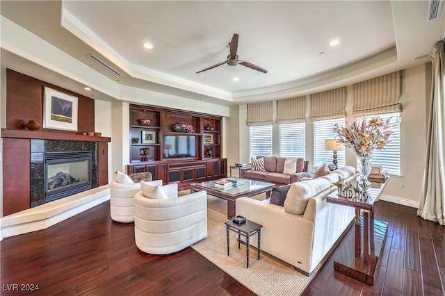 living room with dark wood-type flooring, a fireplace, a tray ceiling, and ceiling fan