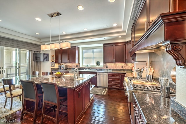 kitchen with dishwasher, an island with sink, decorative light fixtures, dark stone countertops, and dark hardwood / wood-style floors