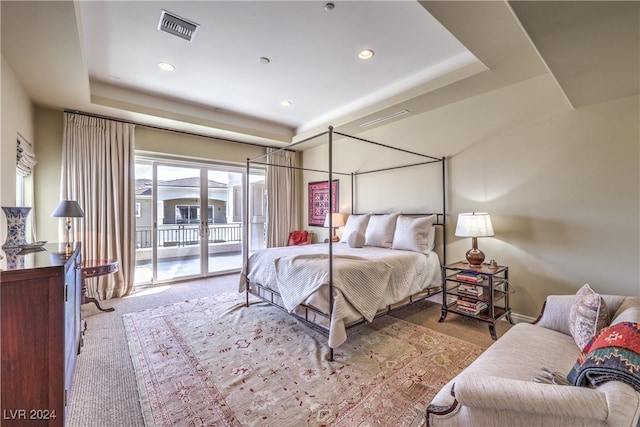 carpeted bedroom with access to exterior and a tray ceiling