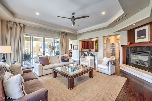 living room featuring light hardwood / wood-style floors, a premium fireplace, a tray ceiling, and ceiling fan