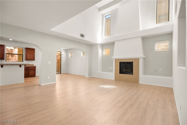 unfurnished living room featuring light wood-type flooring, a tiled fireplace, and a towering ceiling