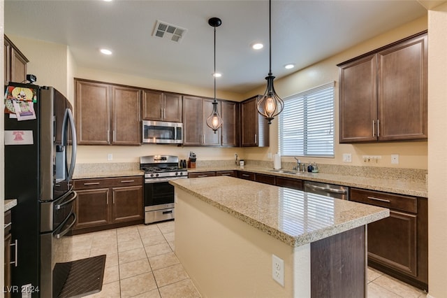 kitchen with light tile patterned flooring, light stone counters, stainless steel appliances, a center island, and decorative light fixtures