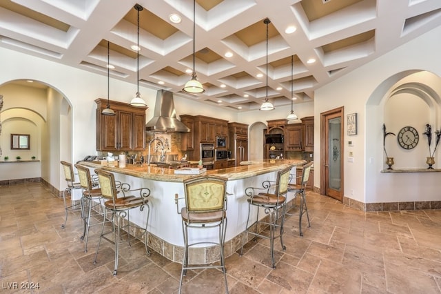 kitchen with a breakfast bar, decorative light fixtures, light stone countertops, and wall chimney range hood