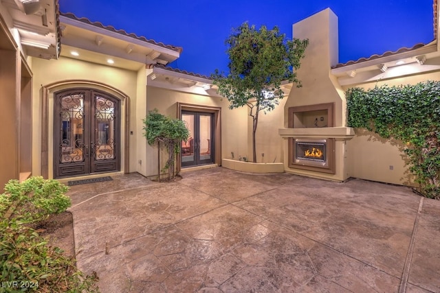 exterior entry at night with an outdoor fireplace, a patio, and french doors