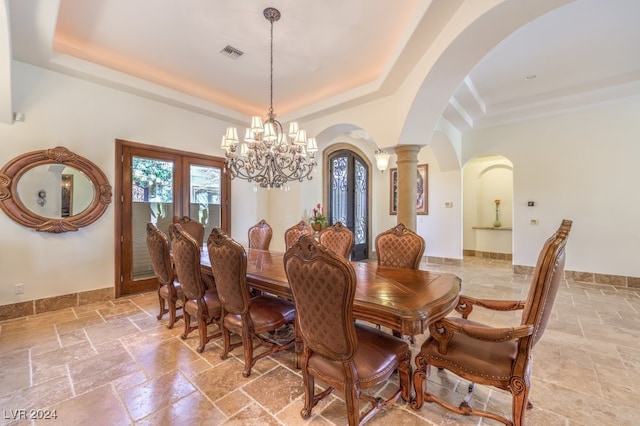 dining area with decorative columns, french doors, a tray ceiling, and a chandelier