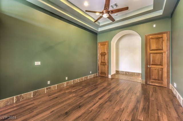 unfurnished room with a tray ceiling, ceiling fan, and dark wood-type flooring