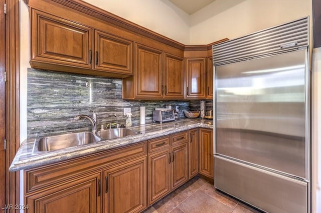 kitchen featuring backsplash, dark tile patterned flooring, sink, stone countertops, and stainless steel built in refrigerator