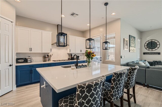 kitchen with pendant lighting, light hardwood / wood-style floors, a kitchen island with sink, sink, and white cabinetry