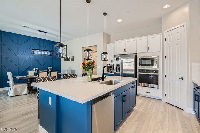 kitchen with white cabinets, pendant lighting, stainless steel appliances, a kitchen island with sink, and sink