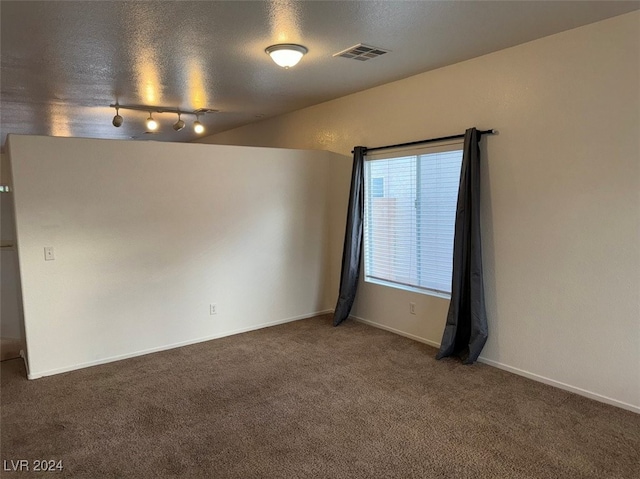 empty room with dark colored carpet, a textured ceiling, and rail lighting