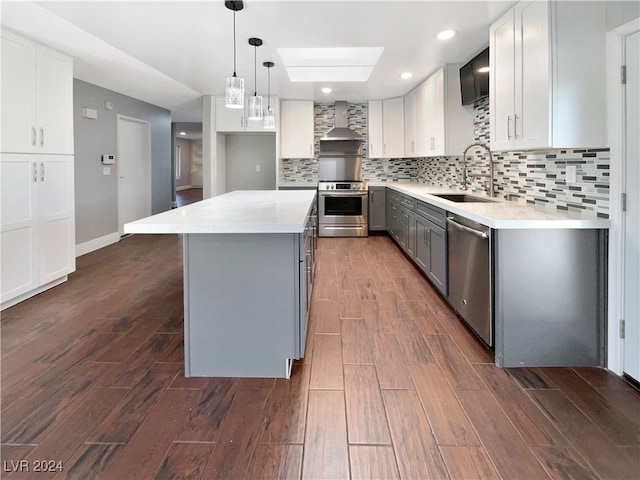 kitchen featuring white cabinets, dark wood-type flooring, wall chimney range hood, appliances with stainless steel finishes, and a center island