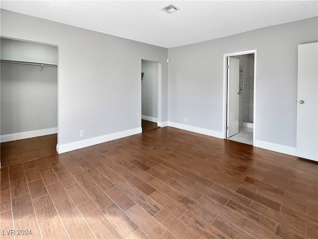 unfurnished bedroom with a textured ceiling, dark hardwood / wood-style floors, a closet, and ensuite bath