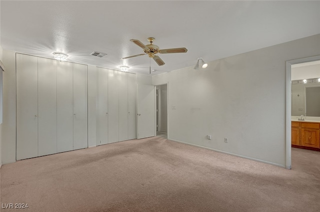 unfurnished bedroom with ceiling fan, light colored carpet, and connected bathroom