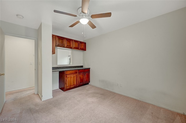 kitchen with ceiling fan, light colored carpet, and built in desk