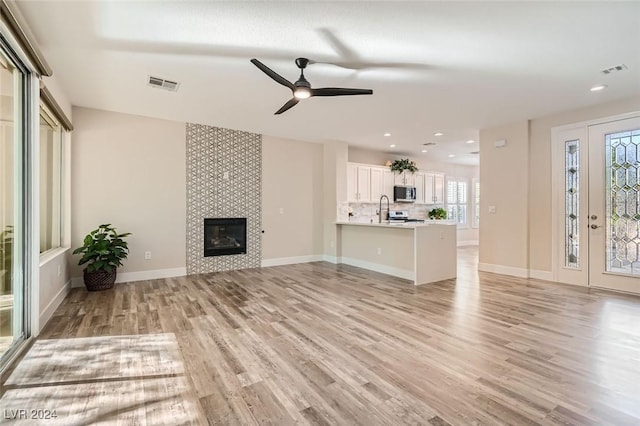 unfurnished living room featuring ceiling fan, sink, a tiled fireplace, and light hardwood / wood-style floors