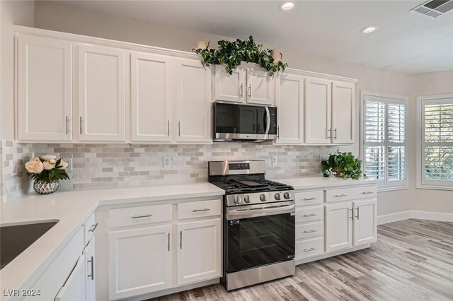 kitchen with tasteful backsplash, stainless steel appliances, light hardwood / wood-style floors, and white cabinets