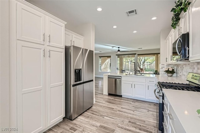 kitchen with sink, appliances with stainless steel finishes, white cabinets, light hardwood / wood-style floors, and backsplash