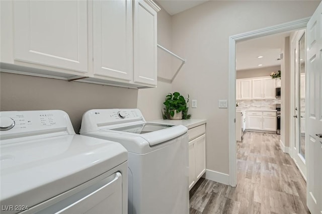 laundry area featuring light hardwood / wood-style flooring, washing machine and dryer, and cabinets