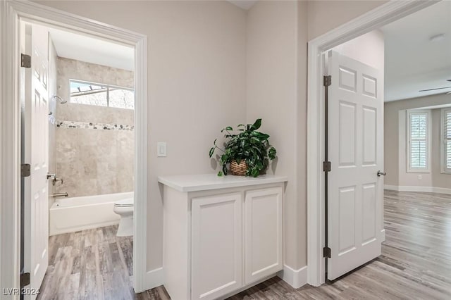 bathroom with ceiling fan, tiled shower / bath, wood-type flooring, and toilet