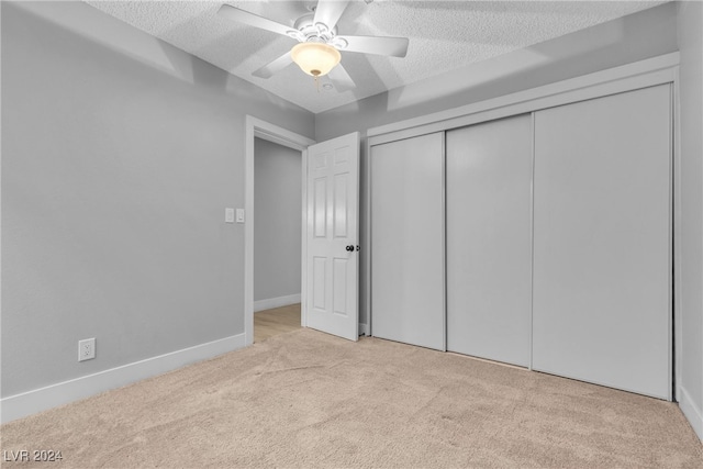 unfurnished bedroom featuring ceiling fan, a closet, light colored carpet, and a textured ceiling