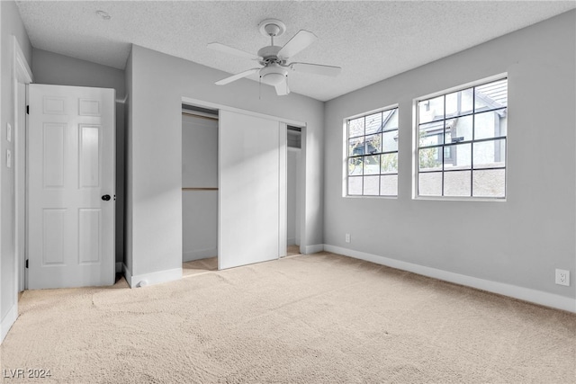 unfurnished bedroom featuring a closet, a textured ceiling, light colored carpet, and ceiling fan