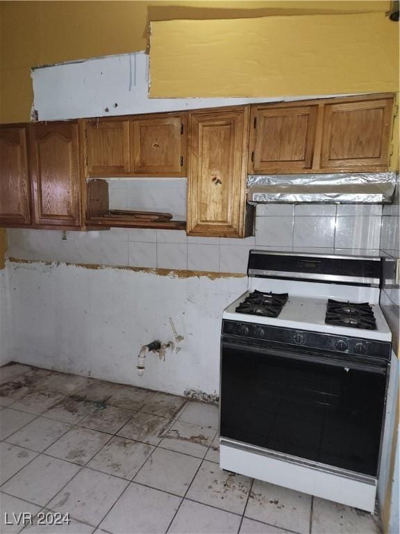 kitchen with tasteful backsplash, range with gas cooktop, brown cabinets, light countertops, and under cabinet range hood