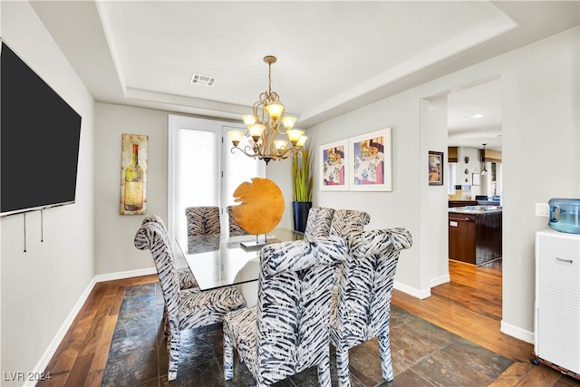 dining room with a chandelier, a raised ceiling, and dark wood-type flooring