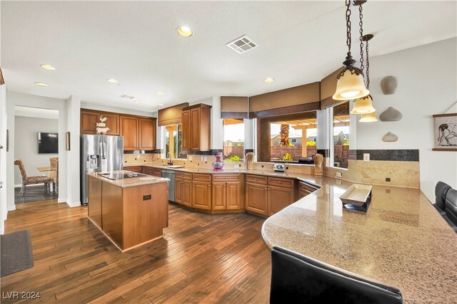 kitchen with light stone countertops, kitchen peninsula, a center island, and dark wood-type flooring