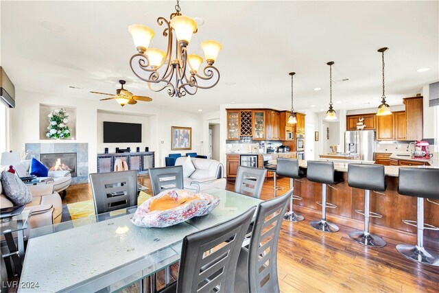 dining room featuring ceiling fan with notable chandelier, light wood-type flooring, a tiled fireplace, and sink