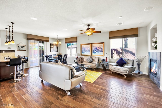 living room with ceiling fan with notable chandelier, dark wood-type flooring, a healthy amount of sunlight, and a tile fireplace