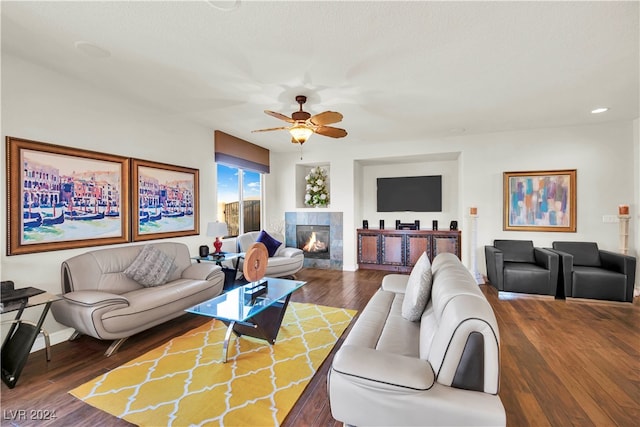 living room featuring ceiling fan, a tiled fireplace, and dark hardwood / wood-style flooring