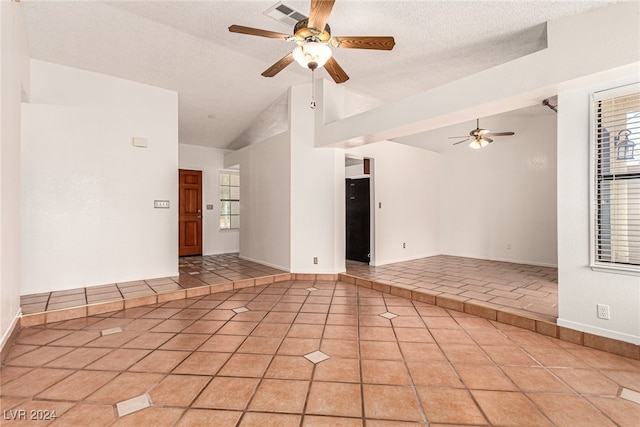 empty room with high vaulted ceiling, ceiling fan, light tile patterned floors, and a textured ceiling