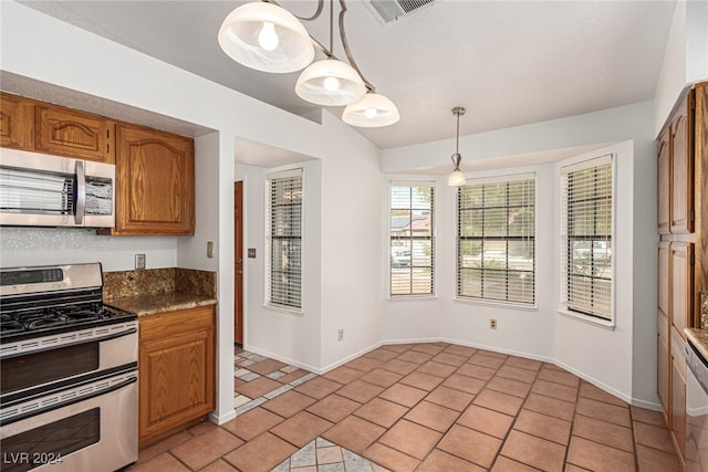 kitchen with decorative light fixtures, stainless steel appliances, light tile patterned floors, and dark stone counters