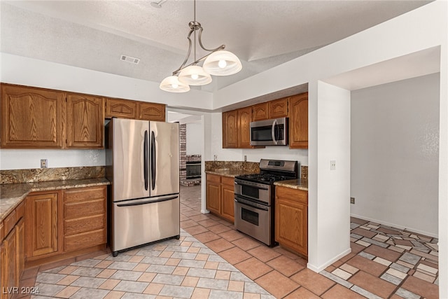 kitchen with light tile patterned flooring, hanging light fixtures, a textured ceiling, appliances with stainless steel finishes, and dark stone counters