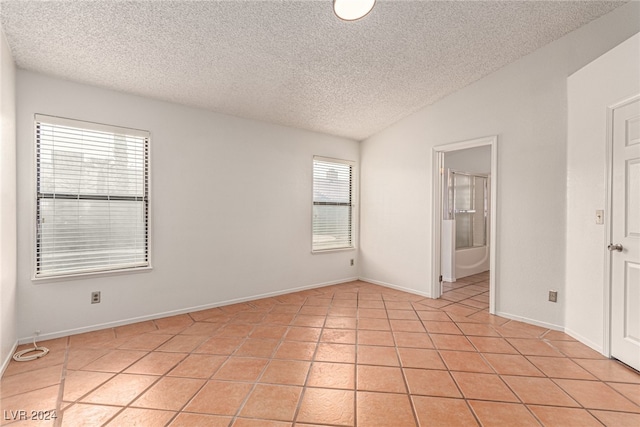 tiled spare room with a textured ceiling, lofted ceiling, and a healthy amount of sunlight