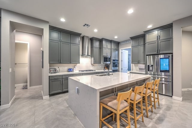 kitchen with an island with sink, sink, wall chimney range hood, appliances with stainless steel finishes, and a breakfast bar area