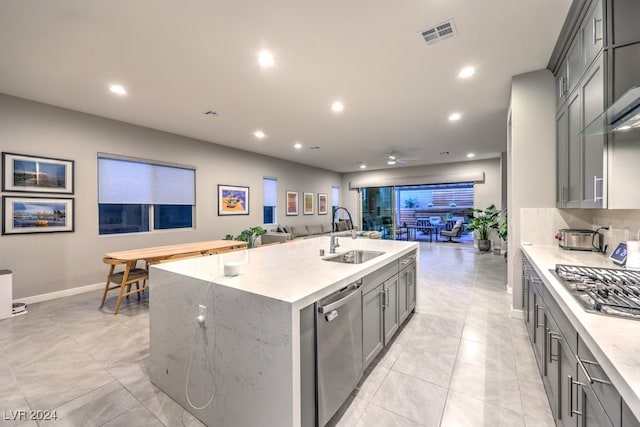 kitchen with gray cabinetry, an island with sink, light stone counters, stainless steel appliances, and sink