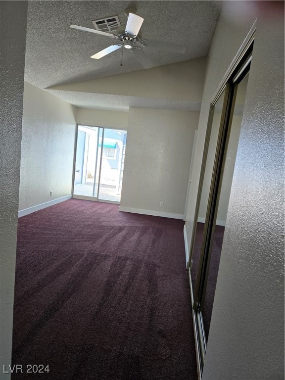 empty room featuring ceiling fan, a textured ceiling, lofted ceiling, and dark carpet