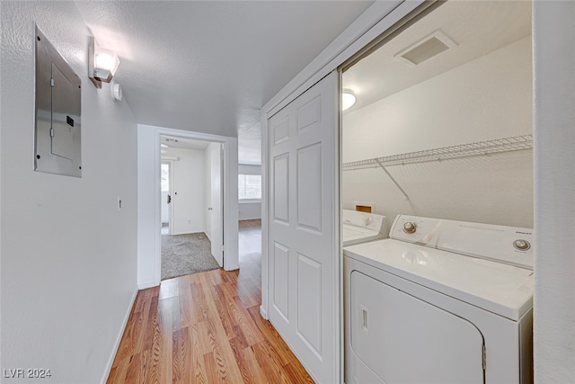 laundry room with independent washer and dryer, light hardwood / wood-style floors, electric panel, and a textured ceiling