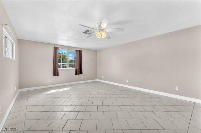 empty room featuring a textured ceiling, light tile patterned floors, and ceiling fan