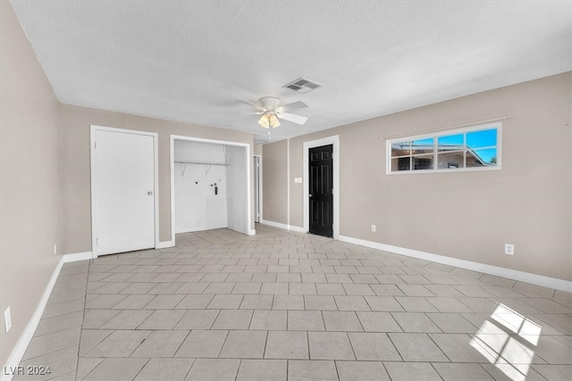 unfurnished bedroom featuring a textured ceiling, light tile patterned flooring, two closets, and ceiling fan