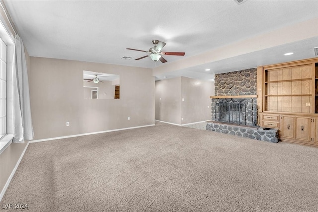 unfurnished living room featuring carpet floors, a stone fireplace, and ceiling fan