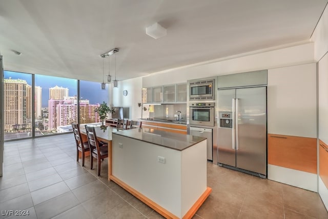 kitchen with a wall of windows, hanging light fixtures, light tile patterned flooring, built in appliances, and sink