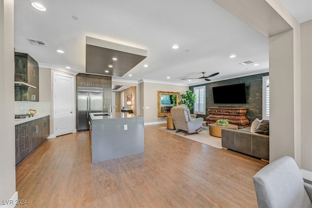 kitchen featuring stainless steel appliances, light wood-type flooring, ceiling fan, a center island with sink, and ornamental molding