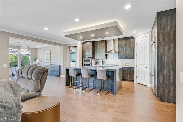 kitchen featuring a kitchen breakfast bar, light hardwood / wood-style floors, dark brown cabinets, a kitchen island with sink, and wall chimney range hood